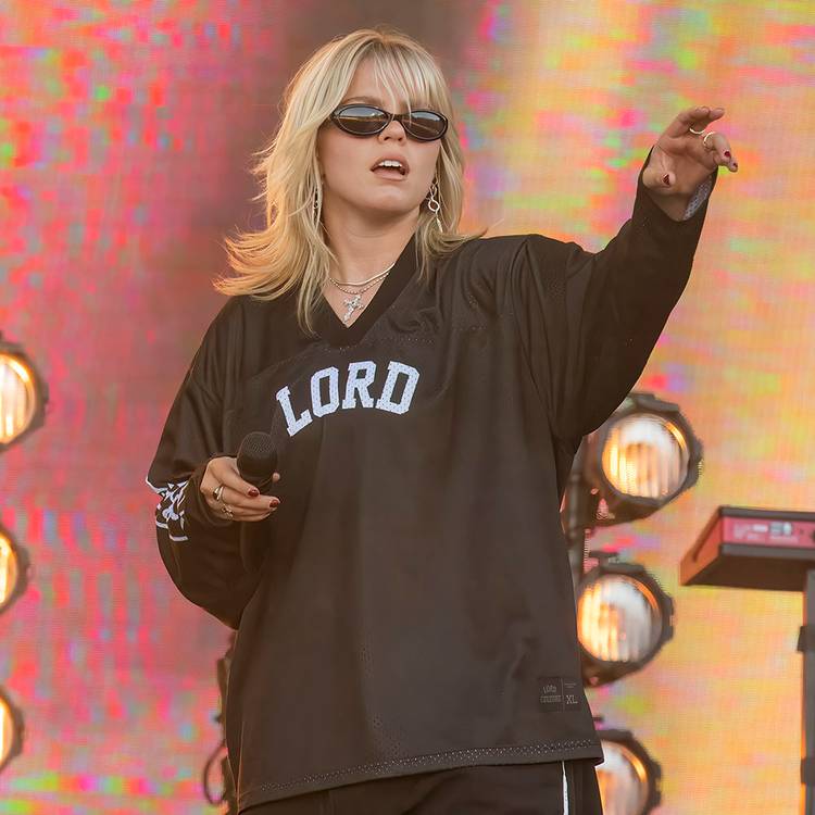 Reneé Rapp performing onstage wearing black shirt and sunglasses