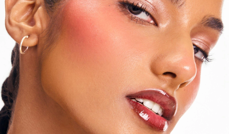 Close-up of a model wearing a glossy rose-brown lip stain with softly defined liner, rosy blush and luminous makeup.