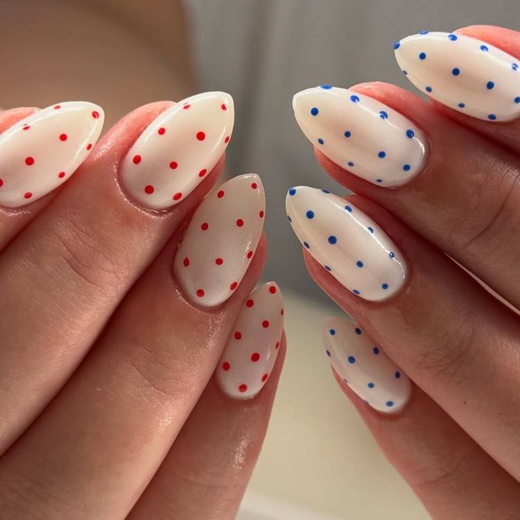 Close-up of almond-shaped milky white nails with scattered red polka dots on one hand and scattered blue polka dots on the other