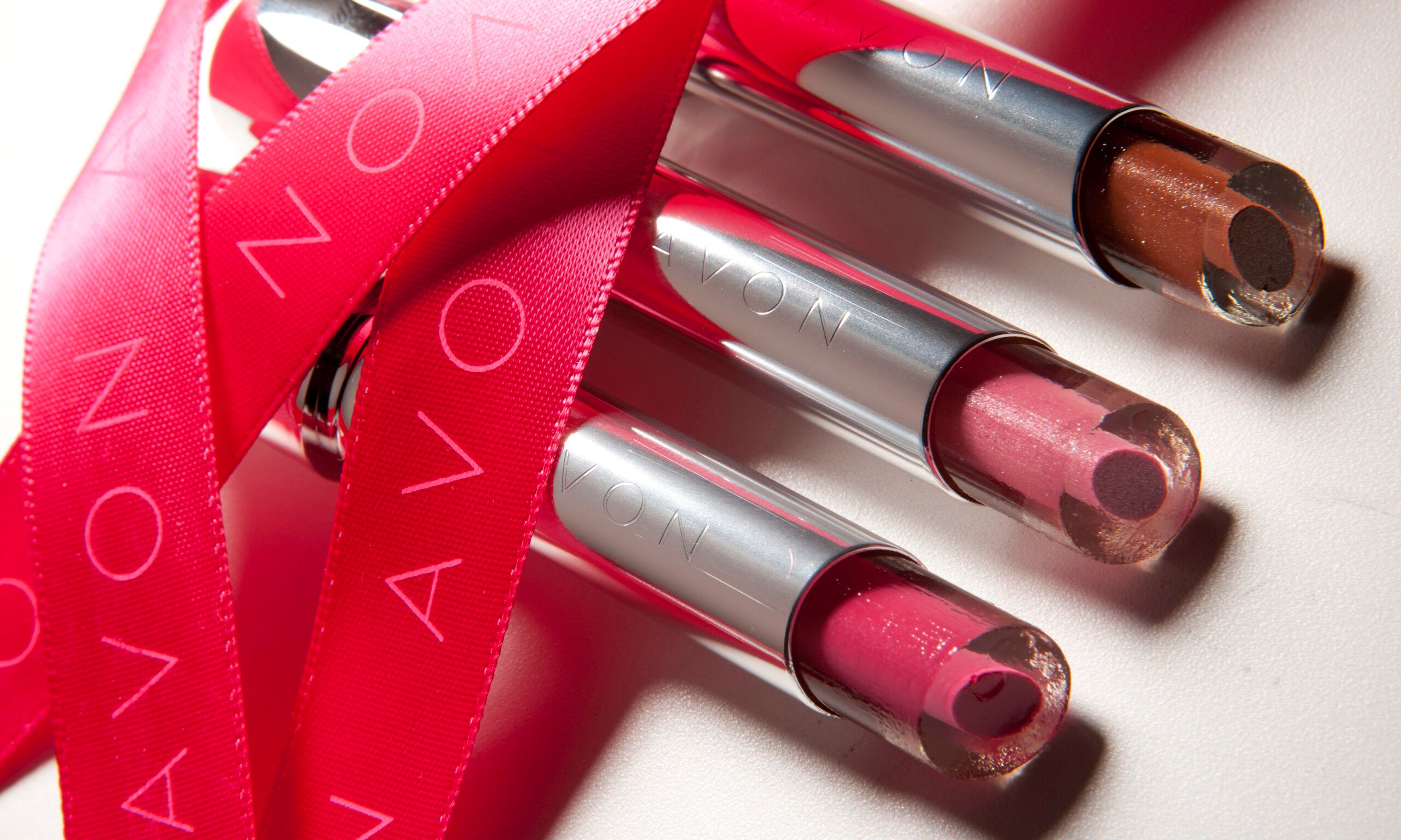 Avon lipsticks are arranged with a red ribbon