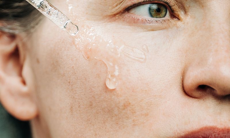 A beautiful woman delicately applies a serum to her cheek using a dropper in a dark, atmospheric setting. This intimate close-up captures self-care, natural beauty routine, and focus on skin health.