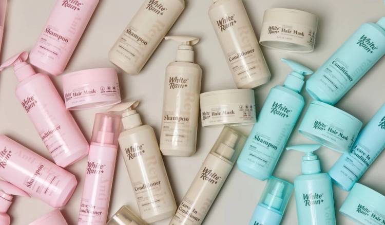 White Rain+ hair-care collection featuring pink Anti-Frizz, cream Repair and blue Volumizing shampoo, conditioner, leave-in conditioner and hair mask bottles arranged on a light background