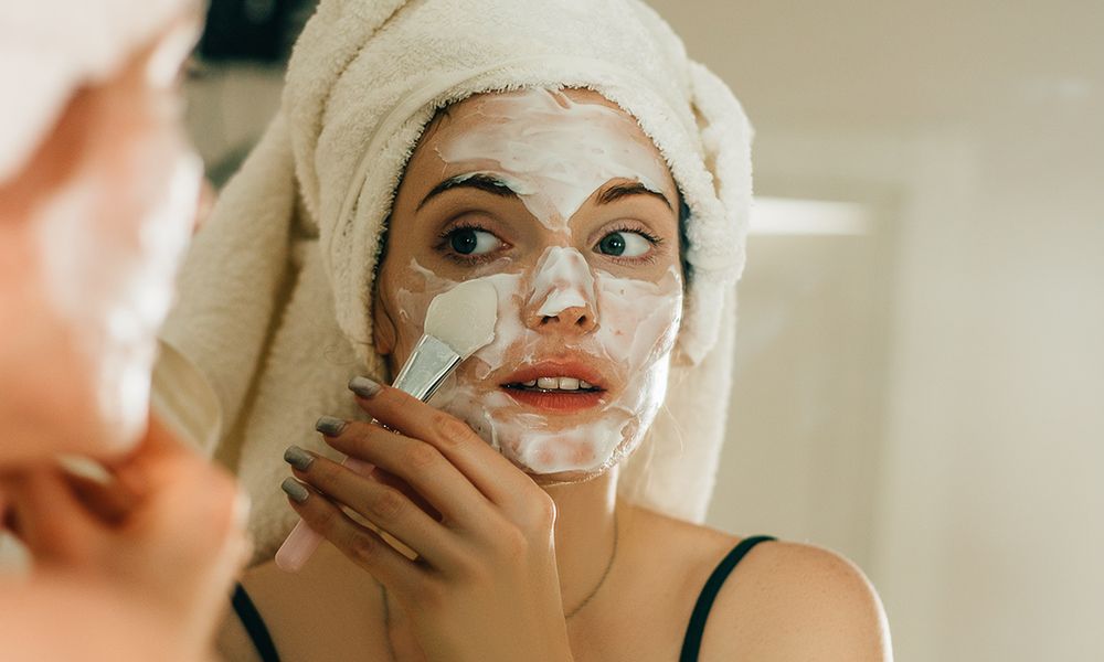 Side view shot of young woman applying facial cosmetic mask in bathroom. Female taking care of her face skin.