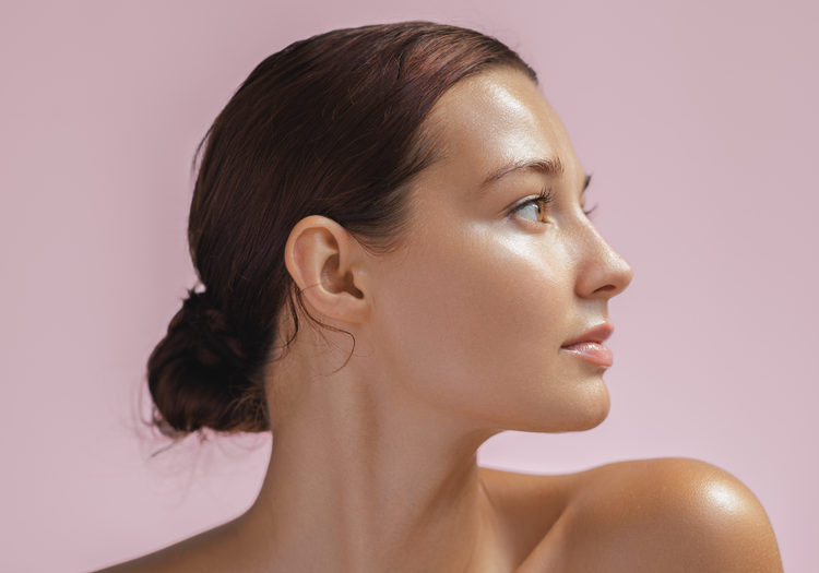 Side-profile portrait of a woman with slicked-back hair and glowing skin, highlighting the jawline and neck.
