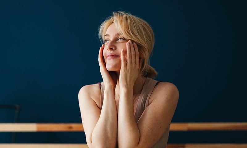 Beautiful blonde woman enjoying waking up in the morning. She is sitting up in her bed and holding her face with her hands.
