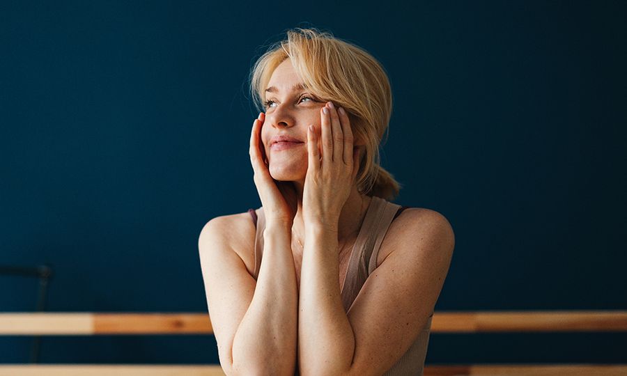 Beautiful blonde woman enjoying waking up in the morning. She is sitting up in her bed and holding her face with her hands.