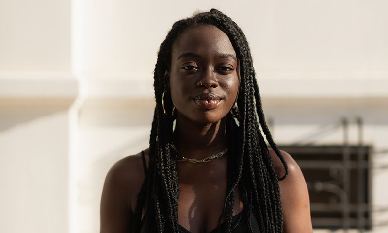 Young black female posing with style while holding her purse and looking at camera in the street during sunset