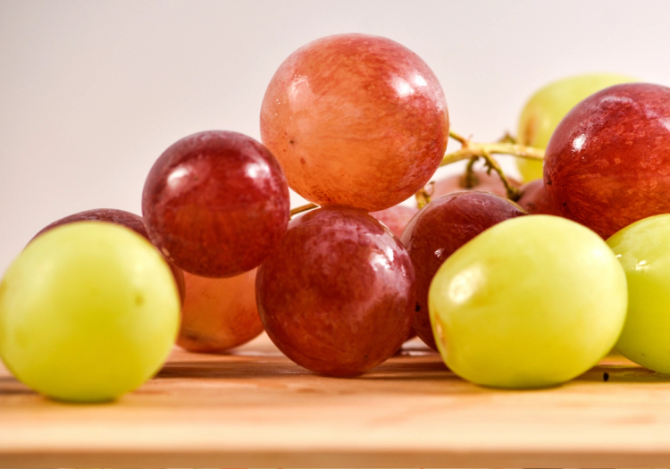 Assorted red and green grapes on a wooden surface, relating to study on grapes and skin protection from UV damage