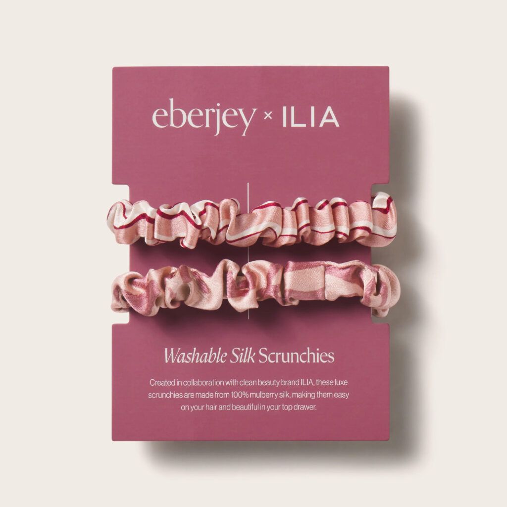 Eberjey x ILIA washable silk scrunchies in pink stripe and palm prints displayed on branded packaging from the Silk Rituals collection.