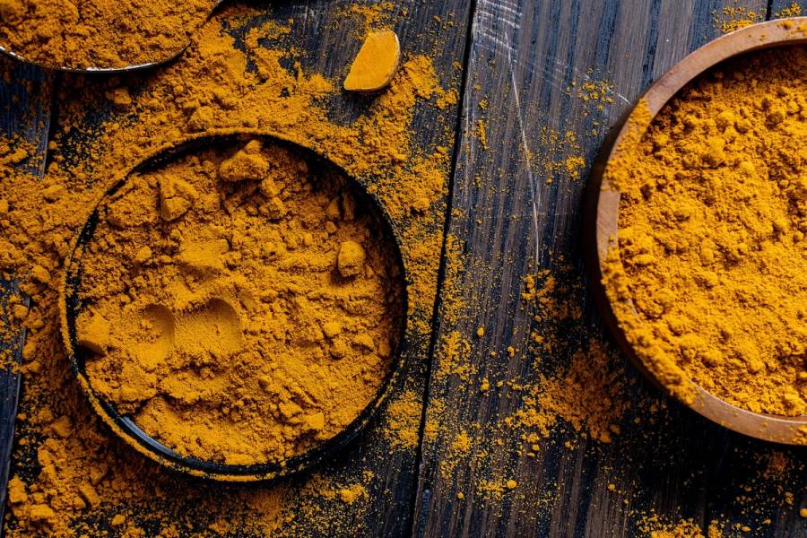 Two bowls of grounded turmeric on a table with some turmeric powder on the table