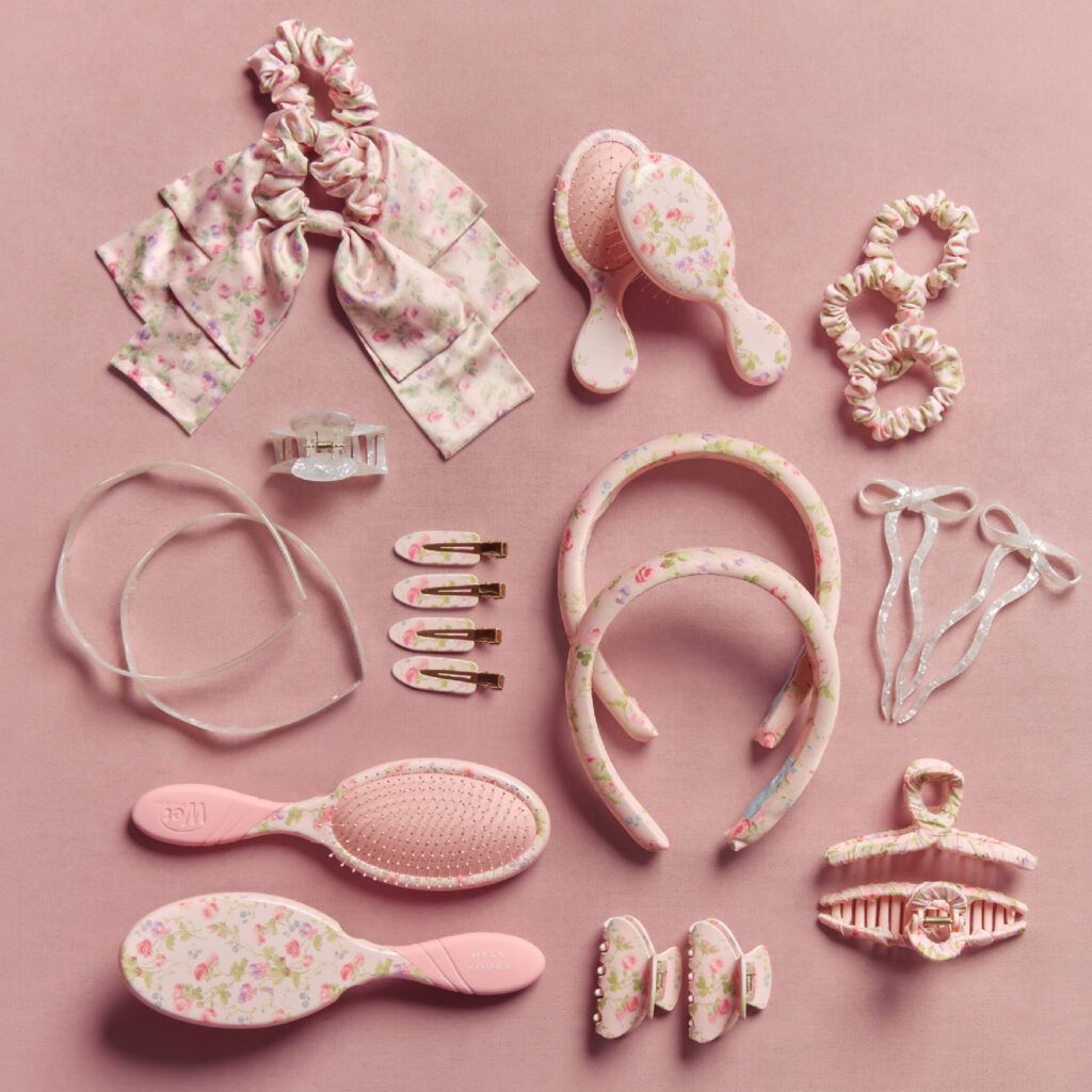 Hill House Home x Wet Brush collaboration featuring pink floral-print hair accessories and brushes—including scrunchies, headbands, claw clips, snap clips and Wet Brush hairbrushes—arranged on a pink background.