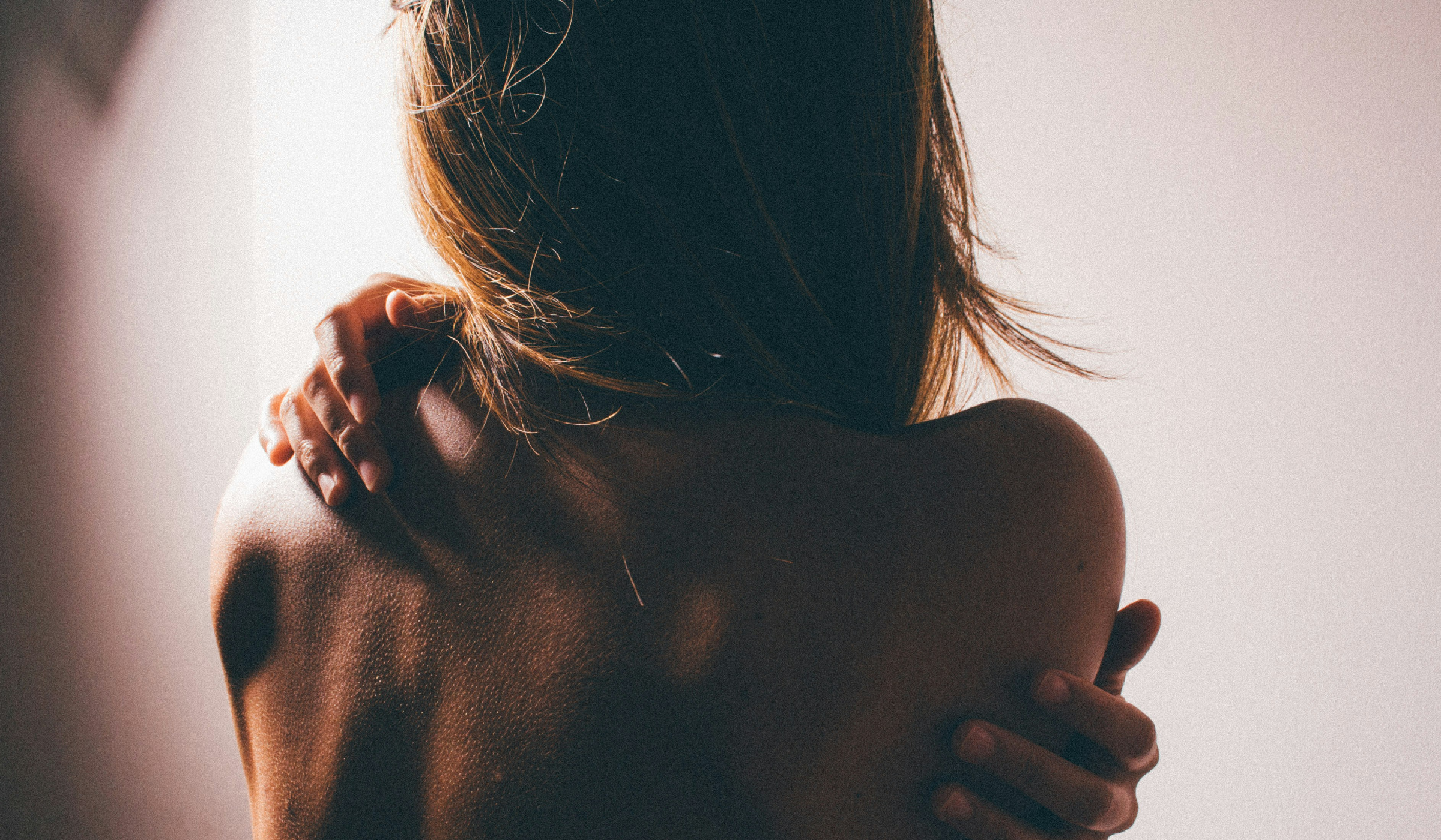 A woman seen from behind with her arms wrapped around her bare shoulders