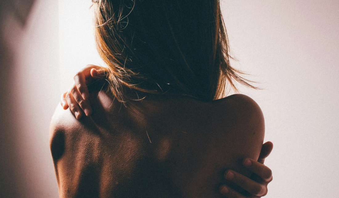 A woman seen from behind with her arms wrapped around her bare shoulders