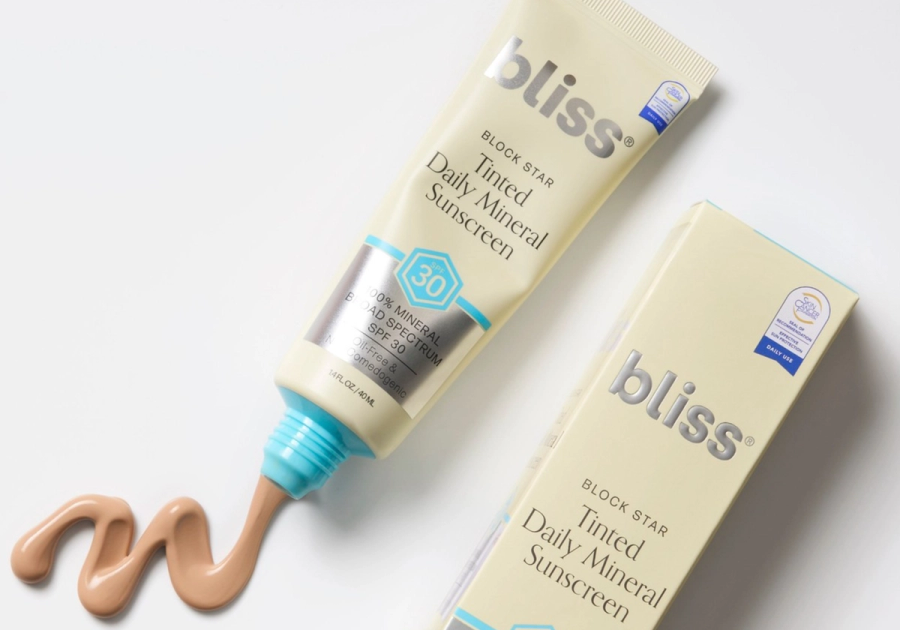Bliss Block Star Tinted Daily Mineral Sunscreen SPF 30 tube and box, with a swirl of tan-toned sunscreen squeezed out to show its blendable texture