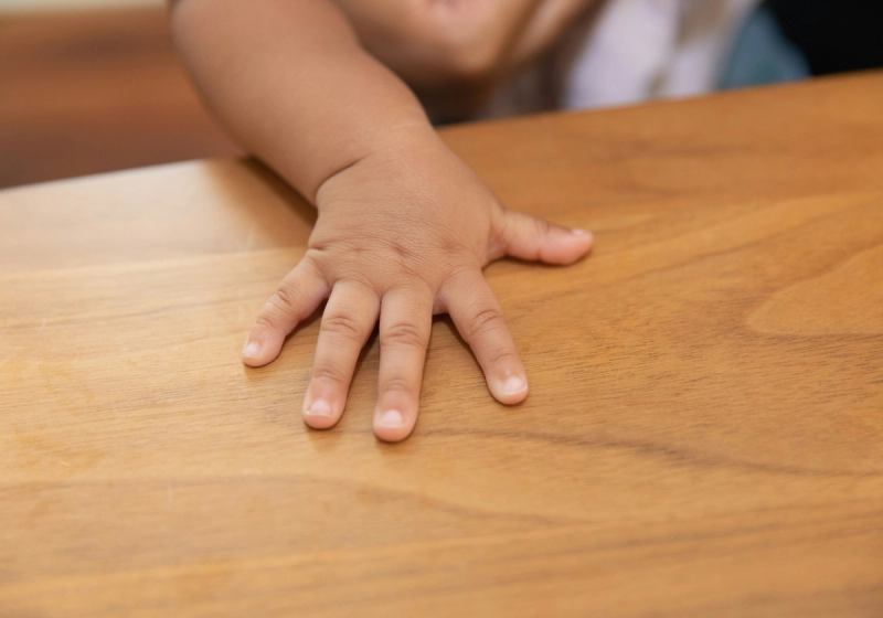 Close-up of a baby's hand resting flat on a wooden table