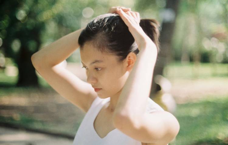 Woman pulling her hair into a ponytail outdoors, part of her scalp visible along the hairline.