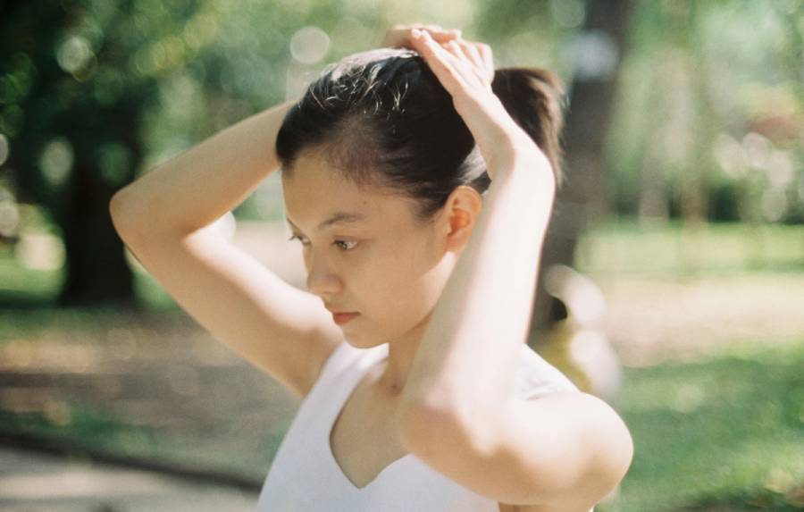Woman pulling her hair into a ponytail outdoors, part of her scalp visible along the hairline.