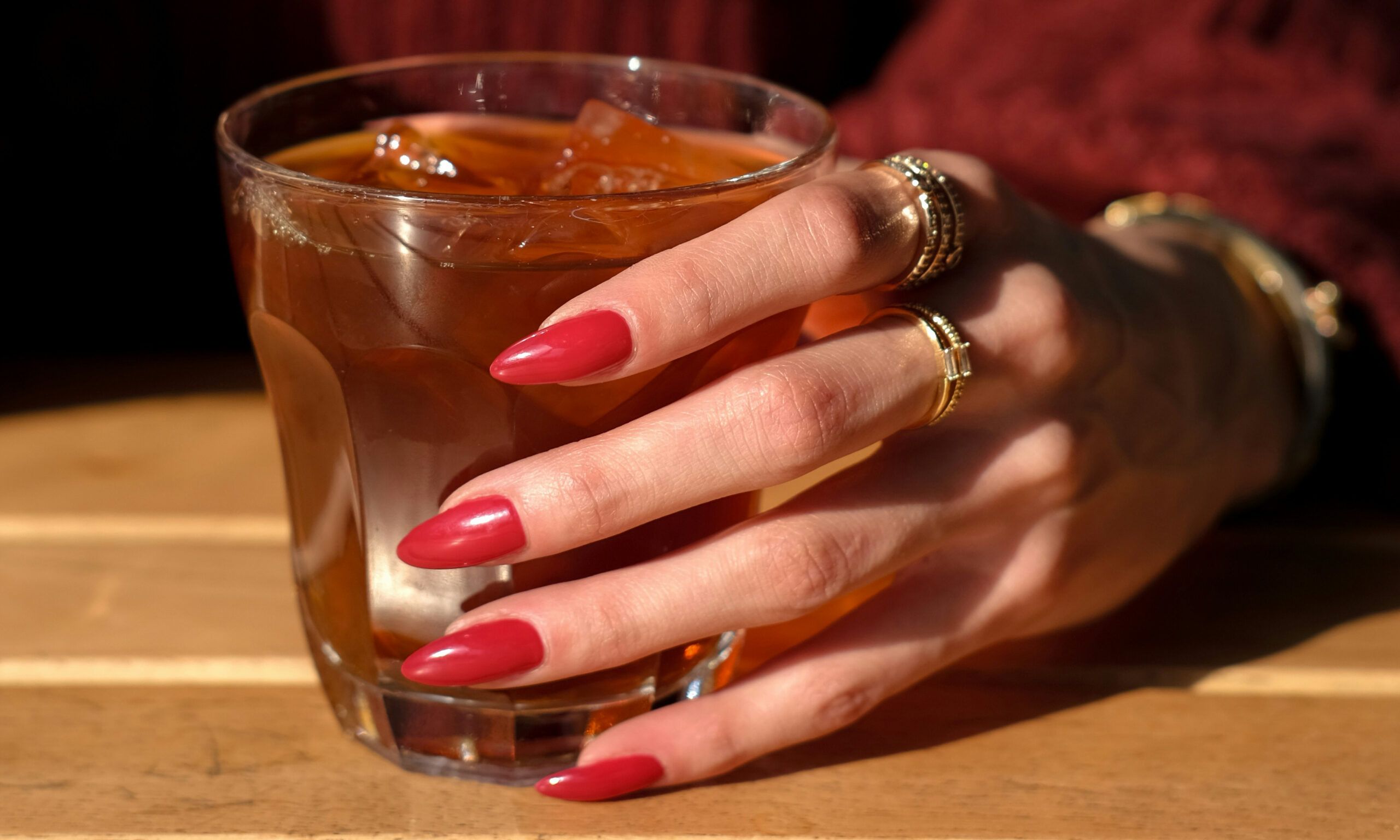 woman with long red nails holding glass of iced tea