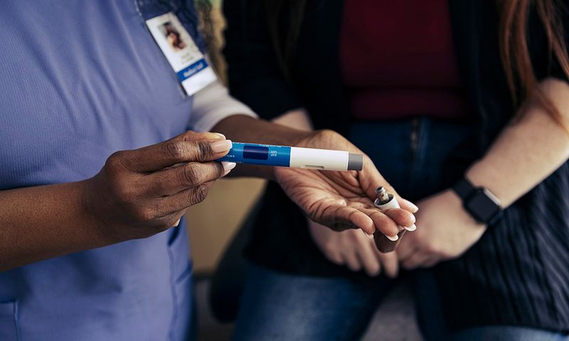 Close-up of nurse's hands holding a medical pen-like device for self-injection. Proper technique is essential for safe medication administration.