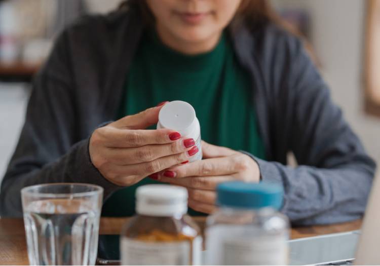 Person holding an over-the-counter medication bottle with pills and water, representing the viral antihistamine trend for PMS and mood symptoms