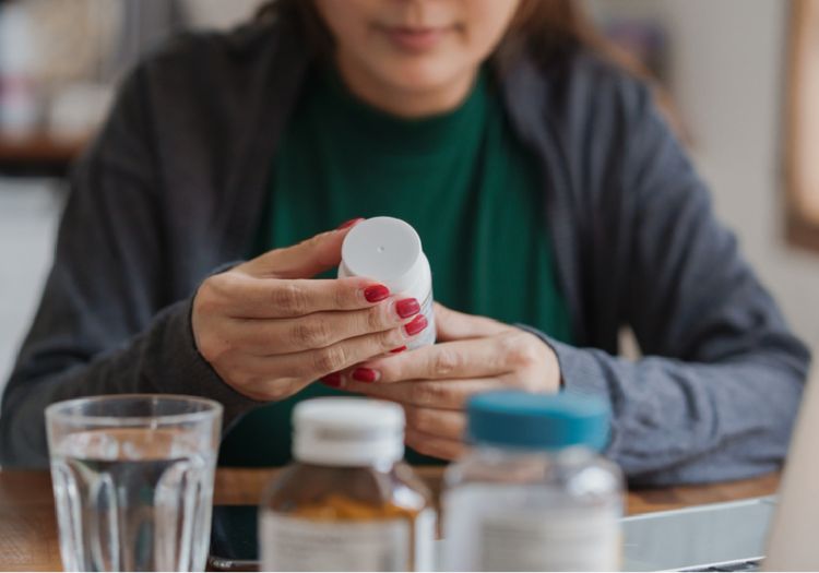 Person holding an over-the-counter medication bottle with pills and water, representing the viral antihistamine trend for PMS and mood symptoms
