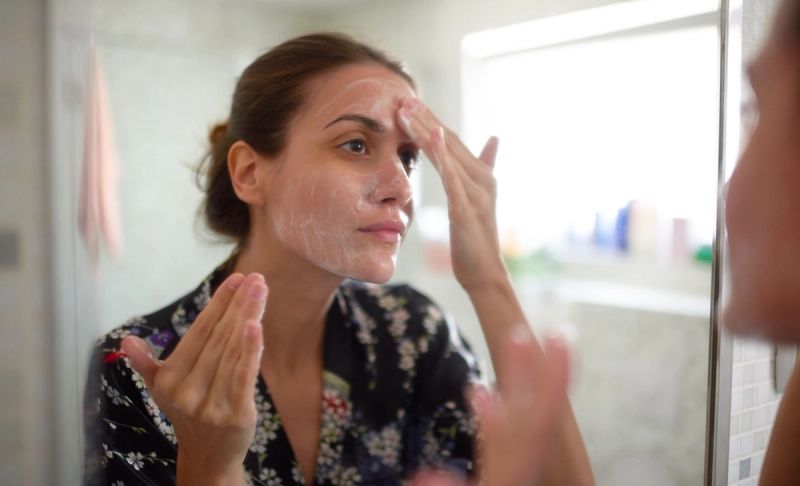 woman applying skin product to face in bathroom