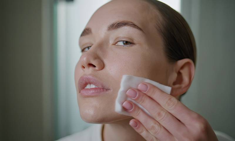Beauty girl applying toner on ideal skin closeup. Attractive model cleansing face looking camera in home bathroom. Young pretty woman removing makeup. Luxury self-care treatment advertisement concept.