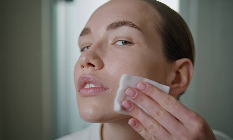 Beauty girl applying toner on ideal skin closeup. Attractive model cleansing face looking camera in home bathroom. Young pretty woman removing makeup. Luxury self-care treatment advertisement concept.