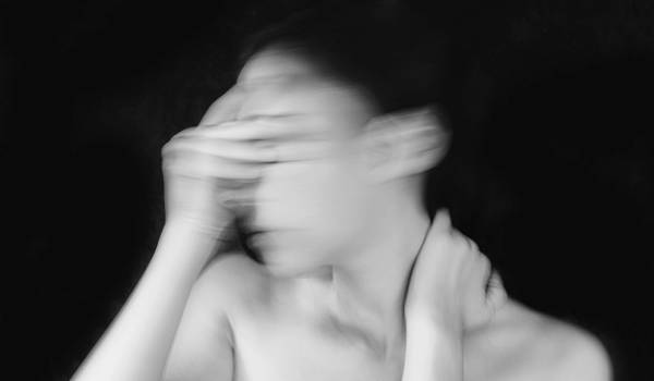 Black-and-white motion-blur portrait of a woman with her hand to her face against a dark background