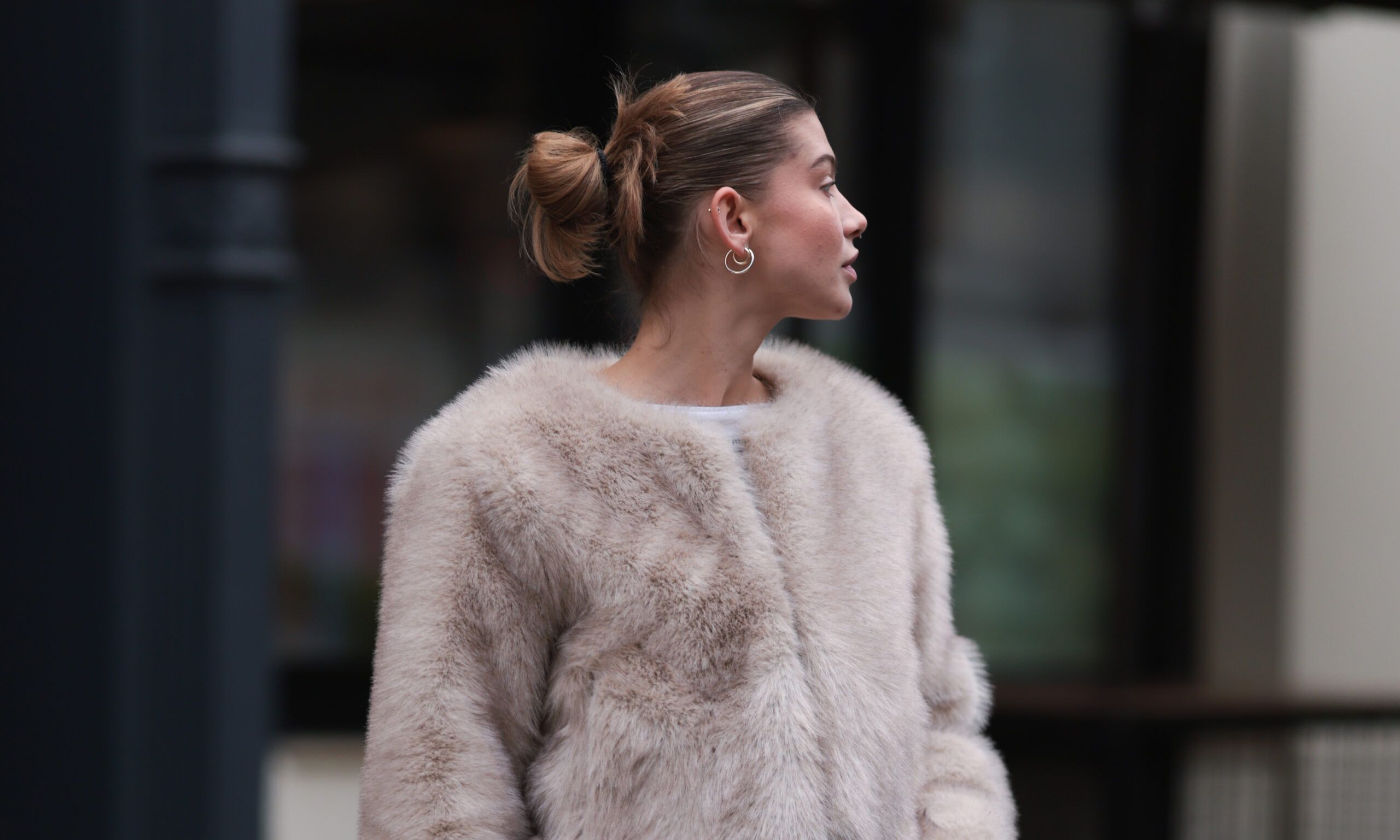 Sophia Geiss is seen wearing two different-sized gold hoop earrings, a silver nose ring, a cropped beige faux fur jacket with wide sleeves from Meotine, underneath a cropped white top from Miu Miu, a brown logo-patterned “Speedy“ bag from Louis Vuitton, a silver ring, wide-legged jeans from COS, and beige suede platform shoes with decorative seams from Ugg on November 22, 2024 in Berlin, Germany.