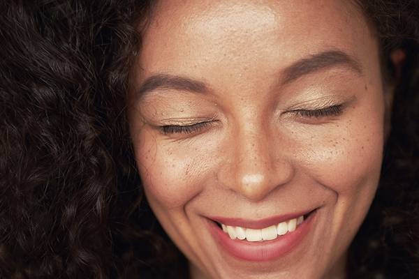 Closeup portrait of beautiful young woman with curly hair style and closed eyes. The woman has white toothy smile and freckles. The mulatto is a representative of a mixed race, an African American and a white race.