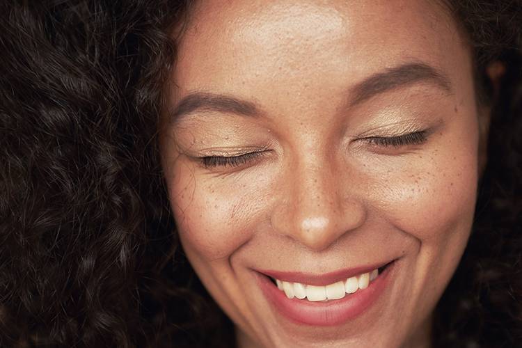 Closeup portrait of beautiful young woman with curly hair style and closed eyes. The woman has white toothy smile and freckles. The mulatto is a representative of a mixed race, an African American and a white race.