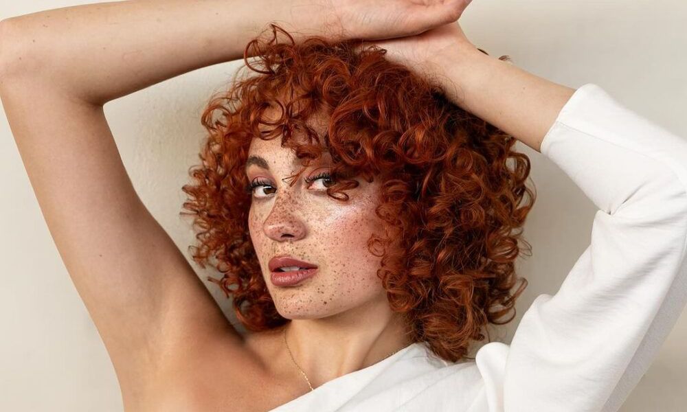 freckle-faced woman with short red curly hair and bangs