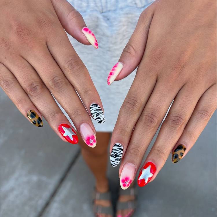 Close-up of two hands with mixed maximalist nail art featuring tie-dye pink tips, a red nail with a silver star, zebra print, leopard print and floral accents on almond-shaped nails