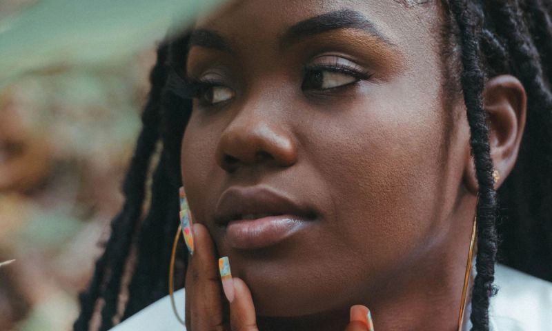A woman with dreadlocks looking away from camera with hand on hr face