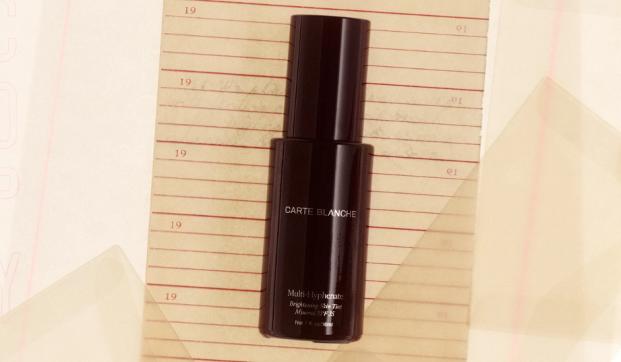 A dark oxblood glass bottle of Carte Blanche's Multi-Hyphenate Brightening Skin Tint Mineral SPF 35 lies on a lined notebook page marked with faded "19" date numbers.