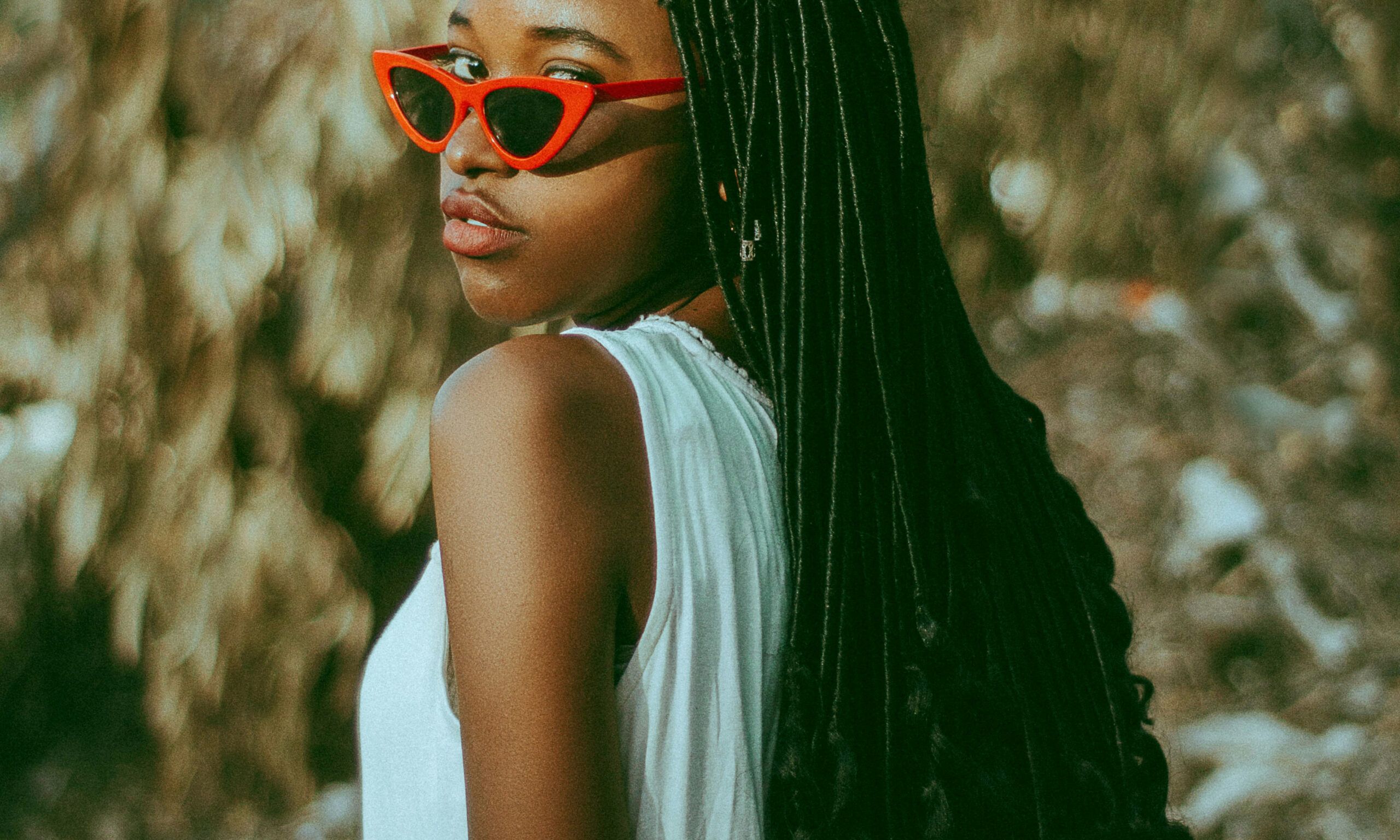 woman with red sunglasses and long braids and curls looking over her shoulder