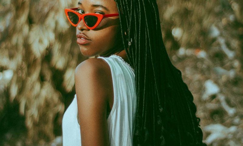 woman with red sunglasses and long braids and curls looking over her shoulder