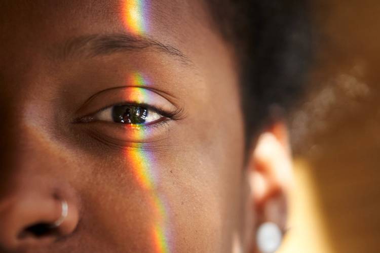 Close-up of a person’s eye and skin with a rainbow light reflection across the face