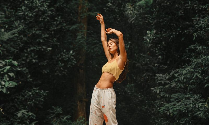 woman in front of trees and bushes with arms up above her head