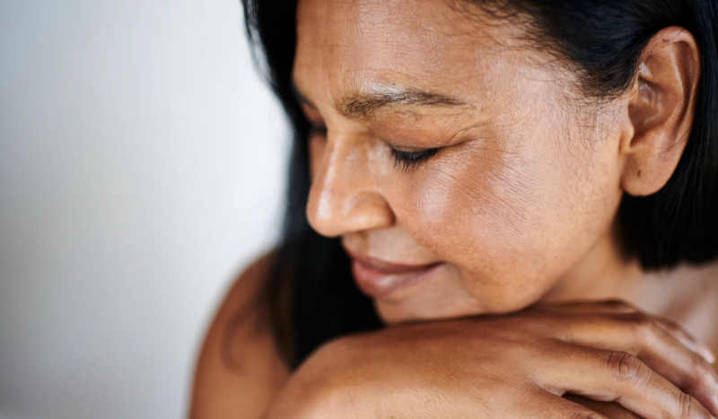 Woman with mature skin and dark hair rests her chin on her hands, eyes closed.