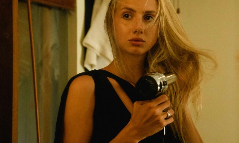 woman looking in mirror blow drying hair