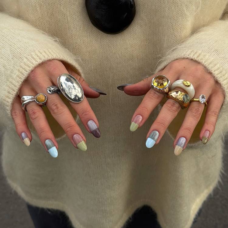 Hands with pastel pill-box-inspired manicures and chunky statement rings against a cream knit sweater.