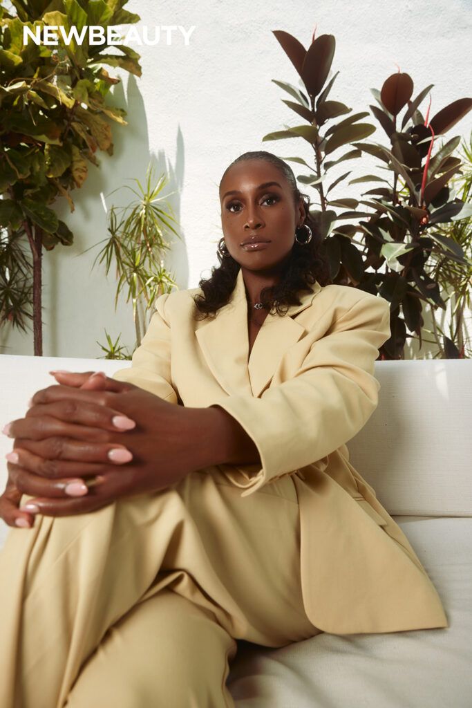 Issa Rae sitting on white sofa in butter yellow suit 