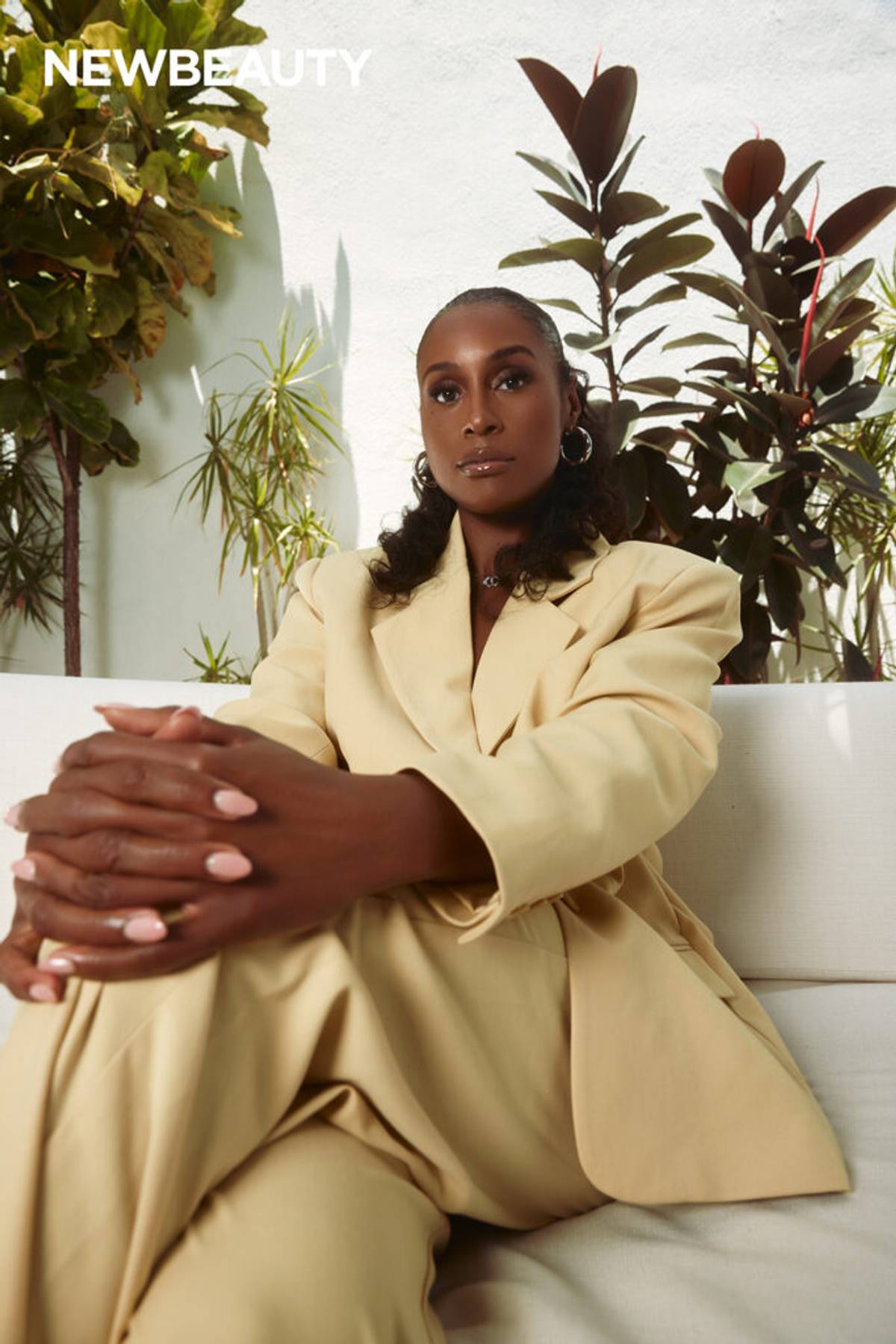 Issa Rae sitting on white sofa in butter yellow suit