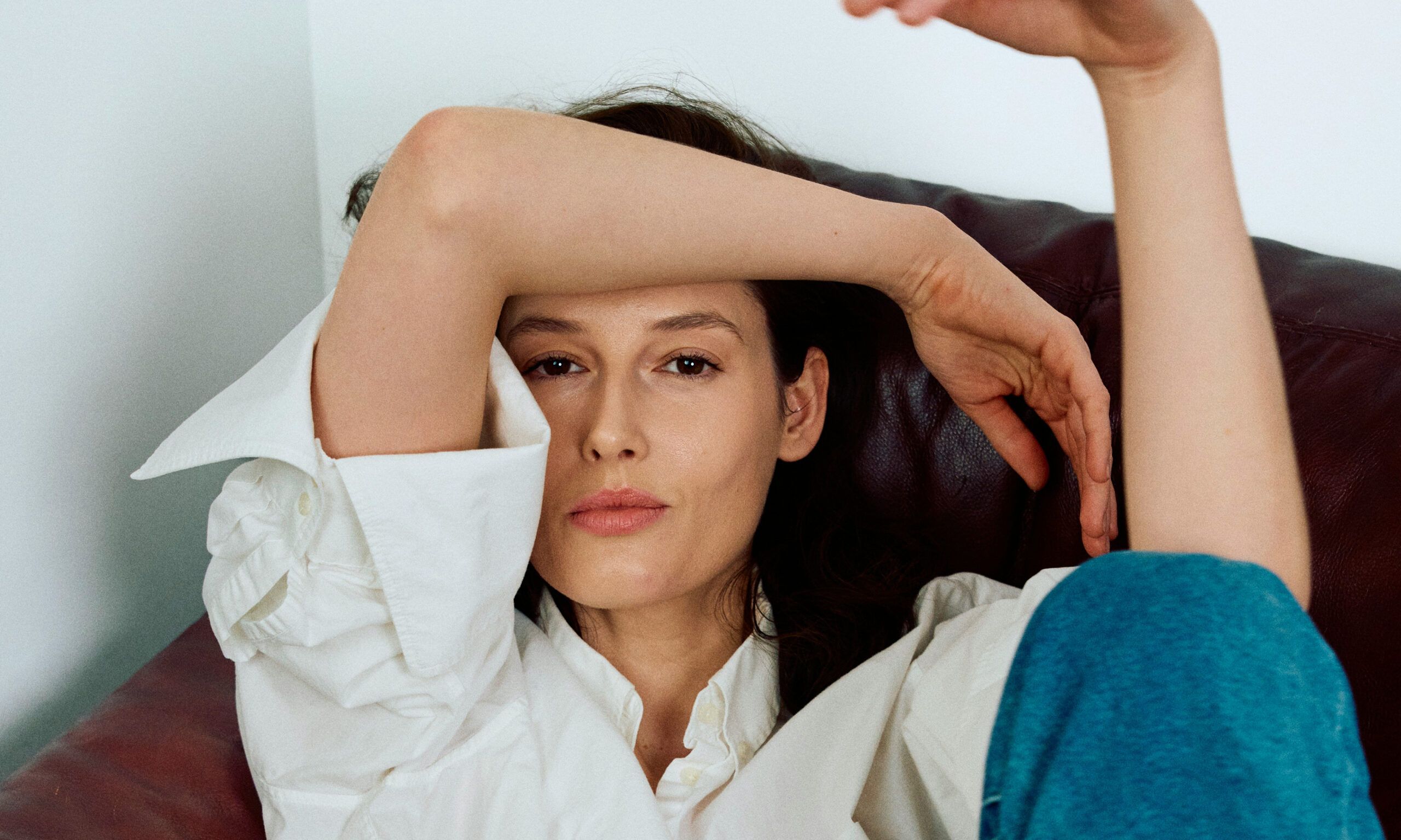 woman in white blouse sitting on couch with arm over her forehead