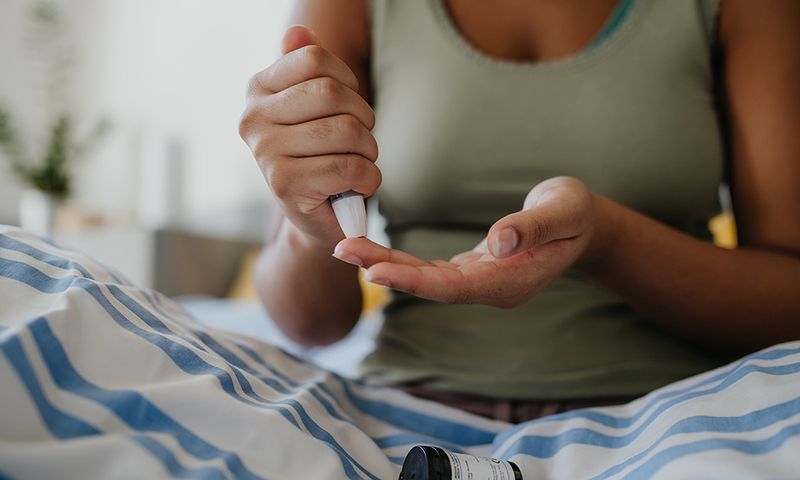 Close up of girl collecting fingerstick blood sample from finger for blood sugar testing at home in the morning. Testing blood sugar levels with a glucometer. Paediatric diabetes in teenage girl and life with chronic illness.