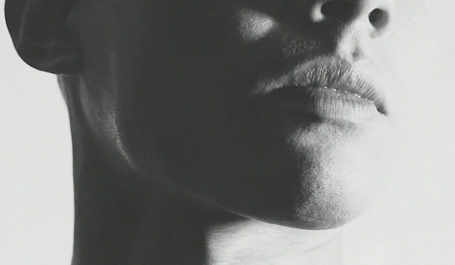 Black-and-white close-up profile shot of a person's lower face, focused on the lips, chin, and jawline, with dramatic high-contrast lighting