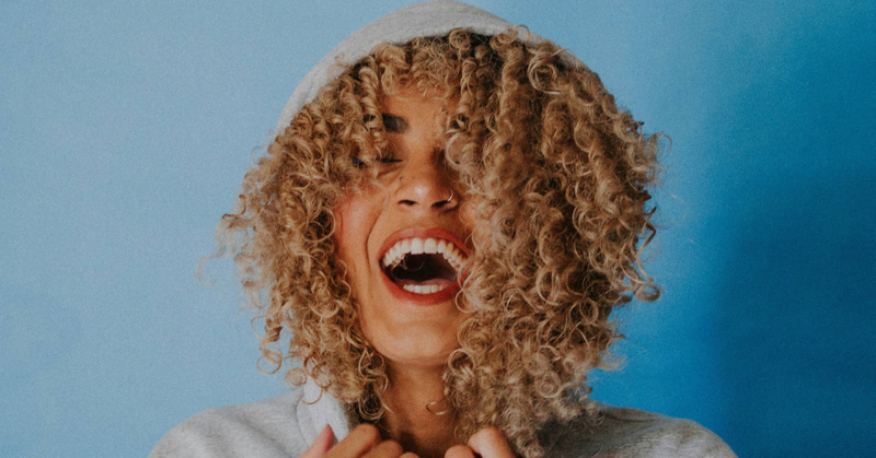 curly haired woman with a hood over her head smiling