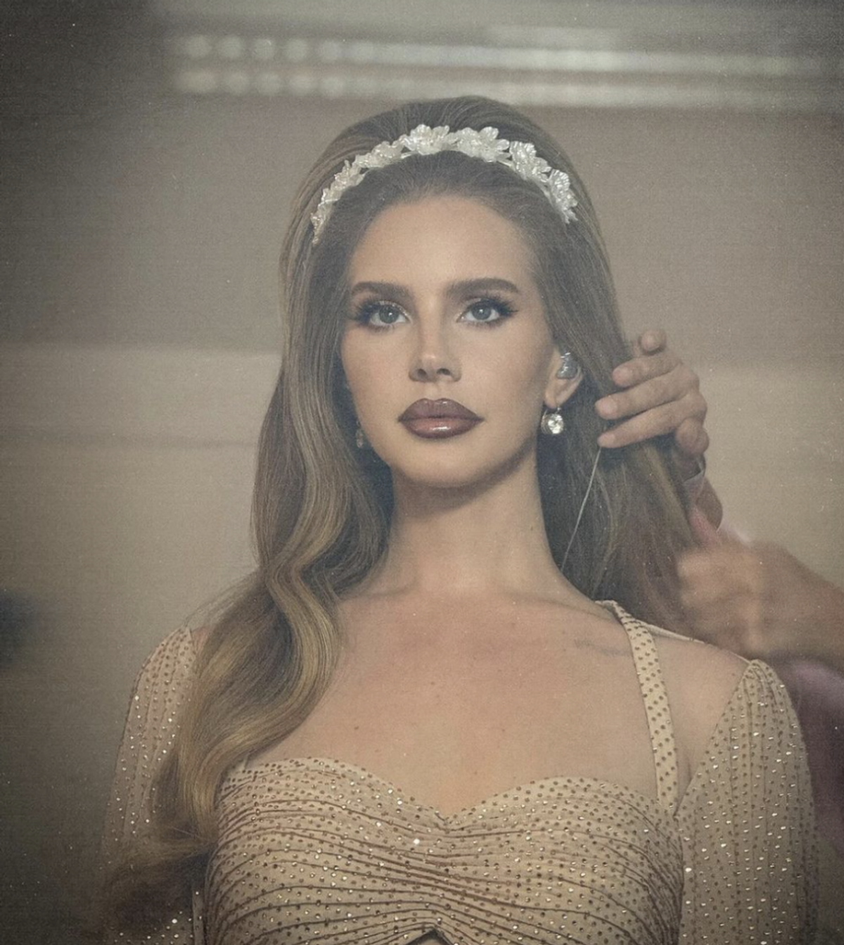 Lana Del Rey getting her hair and makeup done while wearing a gold dress